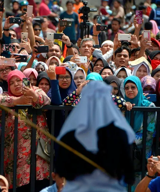 Onlookers hold up smartphones as they witness a public flogging in front of a mosque in the provincial capital Banda Aceh on April 20, 2018. (Photo by Chaideer Mahyuddin/AFP Photo)