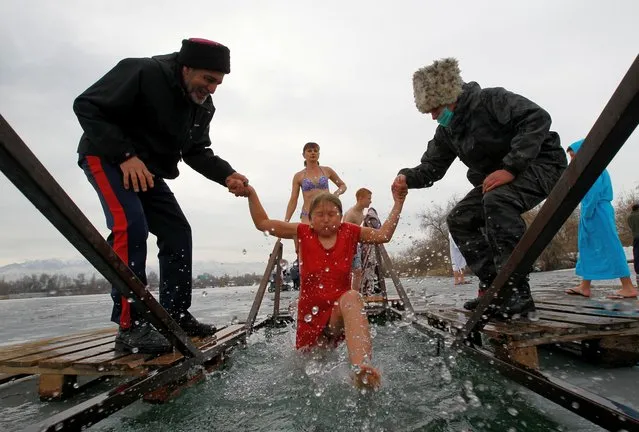 A girl is helped by cossacks while taking a dip in the icy waters during celebrations of the Orthodox Christian feast of Epiphany in the village of Leninskoye, Kyrgyzstan on January 19, 2021. (Photo by Vladimir Pirogov/Reuters)
