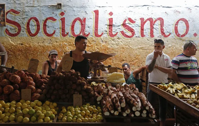 In this December 20, 2014 file photo, workers stand behind their food stalls at a state-run market in Havana, Cuba. The average monthly state salary of $31 is so low that some workers often live on stolen goods and handouts from relatives overseas. (Photo by Desmond Boylan/AP Photo)
