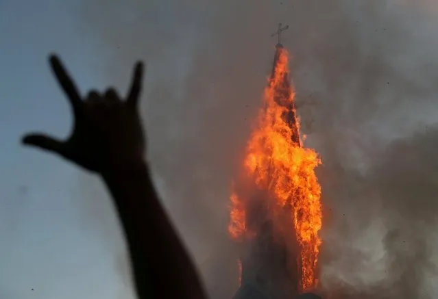 A protester gestures while a church is set on fire during a protest against Chile's government, on the one-year anniversary of the protests and riots that rocked the capital in 2019, in Santiago, Chile, October 18, 2020. (Photo by Ivan Alvarado/Reuters)