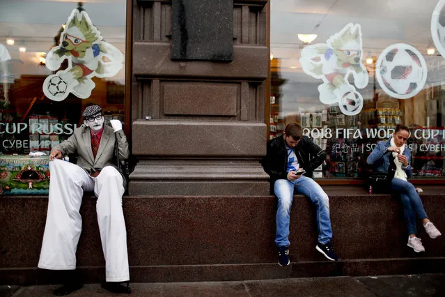 Residents and a street artist sit in a window shop during the 2018 soccer World Cup in St. Petersburg, Russia, Sunday, July 8, 2018. (Photo by Natacha Pisarenko/AP Photo)