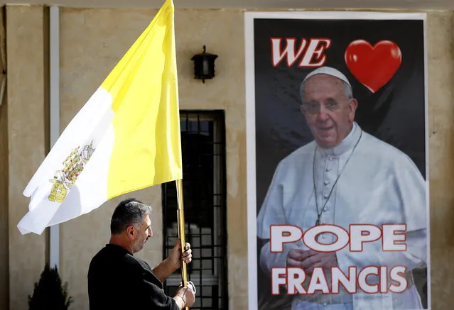 A Christian priest holds a Vatican flag as he walks by a poster of Pope Francis during preparations for the Pope's visit in Mar Youssif Church in Baghdad, Iraq, Friday, February 26, 2021. (Photo by Hadi Mizban/AP Photo)