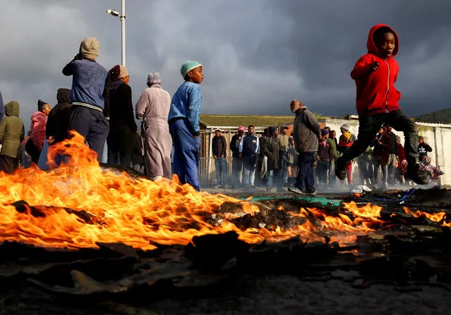 A boy runs past a burning barricade where residents from Overcome Heights, an informal settlement on the Cape Flats, protest over housing in Cape Town, South Africa on July 28, 2023. (Photo by Esa Alexander/Reuters)