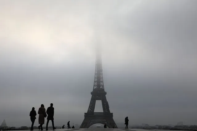 People walk on trocadero plaza in front of the Eiffel tower in the fog on december 19, 2017, in Paris. (Photo by Ludovic Marin/AFP Photo)