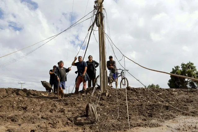 Locals gather next to a damaged electric pole at the shore of a flooded river at Copiapo city, March 26, 2015. (Photo by Ivan Alvarado/Reuters)