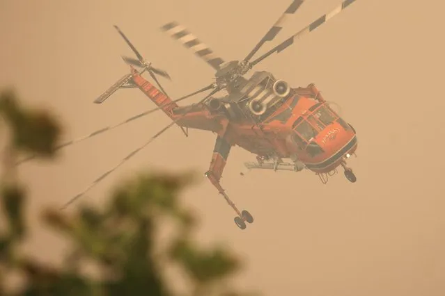 A firefighting helicopter flies over a wildfire burning in the village of Galatsona, on the island of Evia, Greece, August 9, 2021. (Photo by Nicolas Economou/Reuters)