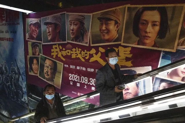 Men wearing masks pass by an advertisement for the patriotic movie “My People, My Parents” at a cinema in Beijing, China, Friday, October 8, 2021. China saw a major dip in travel over the past week's National Day vacation. People staying home appeared to have chosen the cinema instead, with a patriotic Korean War film taking in more than 3.45 billion yuan ($535 million) at the box office. (Photo by Ng Han Guan/AP Photo)