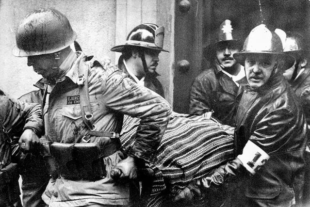 Soldiers and firefighters carry the body of Chilean President Salvador Allende, wrapped in a Bolivian poncho, out of La Moneda presidential palace after it was bombed during a coup by Gen. Augusto Pinochet in Santiago, Chile, September 11, 1973. (Phoot by El Mercurio/AP Photo)