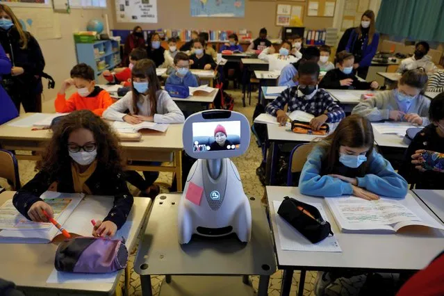Children work in a classroom while a schoolgirl at home, is connected with a “Buddy” tele-education robot at Jules Ferry elementary school on December 3, 2021 in Ormesson-sur-Marne, near Paris. (Photo by Ludovic Marin/AFP Photo)