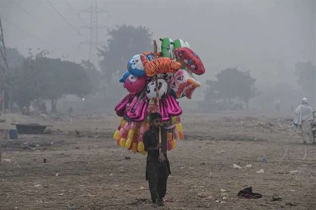 A young street vendor carries balloons as he waits for customers amid smoggy conditions in Lahore on December 2, 2021.  (Photo by Arif Ali/AFP Photo)