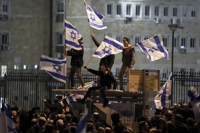 Israeli nationalists weave flags during a protest outside the parliament building in Jerusalem, calling on the government not to demolish a West Bank settlement outpost, Thursday, January 13, 2022. (Photo by Ariel Schalit/AP Photo)