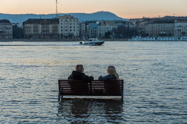 Women sit on a bench surrounded by flood water of the River Danube in Budapest on December 28, 2023, as the lower quays of the riverbank are underwater due to flooding. Due to unusually wet and warm weather in recent days, the River Danube burst its banks in Budapest on December 28. (Photo by Ferenc Isza/AFP Photo)