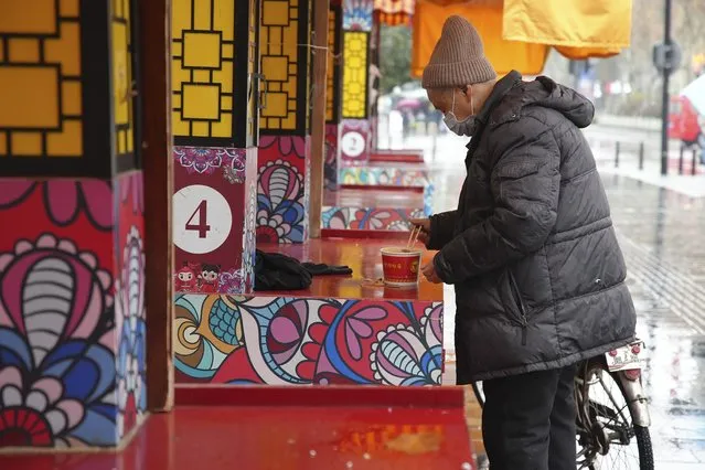 A man wearing a face mask to help protect against COVID-19 prepares to eat noodles on the street of Wuhan in central China's Hubei Province, Sunday, Jan. 23, 2022. Sunday will mark two years since the city of Wuhan was placed under a 76-day lockdown as China tried to contain the first major outbreak of the coronavirus pandemic. (Photo by AP Photo/Stringer)