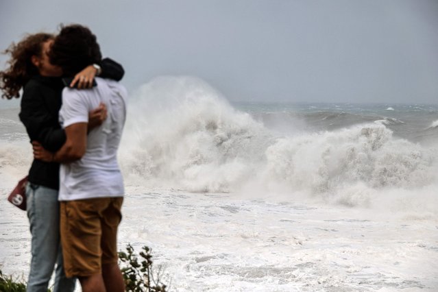 A couple kiss as strong waves hit the coast in Saint-Benoit, on the east of the French Indian Ocean island of La Reunion, on February 2, 2022, ahead of the passage of tropical cyclone Batsirai. La Reunion goes on red alert at 7 pm on February 2, to prepare for the likely passage of cyclone Batsirai overnight. The cyclone already left at least 7,500 homes in nearby Mauritius without power, after it brought heavy downpours and winds of around 120 kilometres per hour, knocking down trees onto electricity lines, according to the local electricity board. (Photo by Richard Bouhet/AFP Photo)
