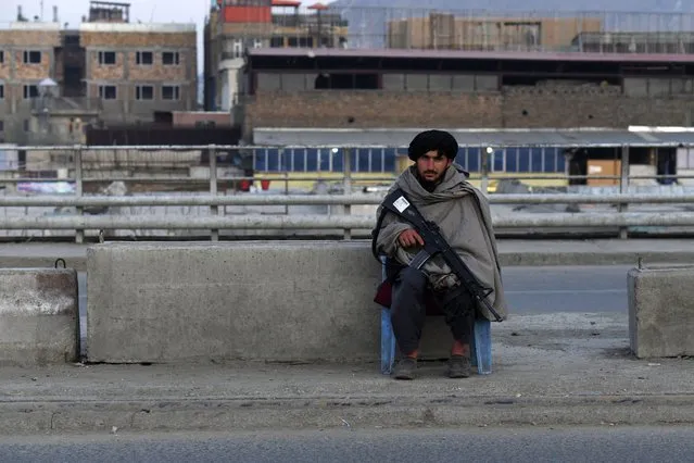 A Taliban fighter sits guard on a road in Kabul on February 20, 2022. (Photo by Sahel Arman/AFP Photo)
