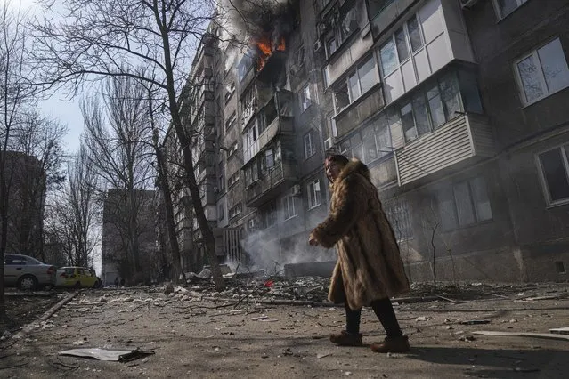 A woman walks past a burning apartment building after shelling in Mariupol, Ukraine, Sunday, March 13, 2022. (Photo by Evgeniy Maloletka/AP Photo)