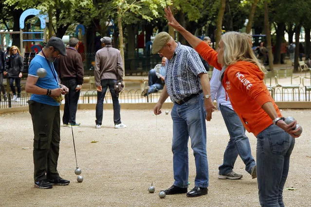 In this Tuesday, June 23, 2015 photo, Andrea throws a boule during an amateur Petanque match in Paris. In the game, the goal is to throw hollow metal balls as close as possible to a small wooden ball, called a “cochonnet” (piglet), while standing inside a circle with both feet on the ground. (Photo by Francois Mori/AP Photo)