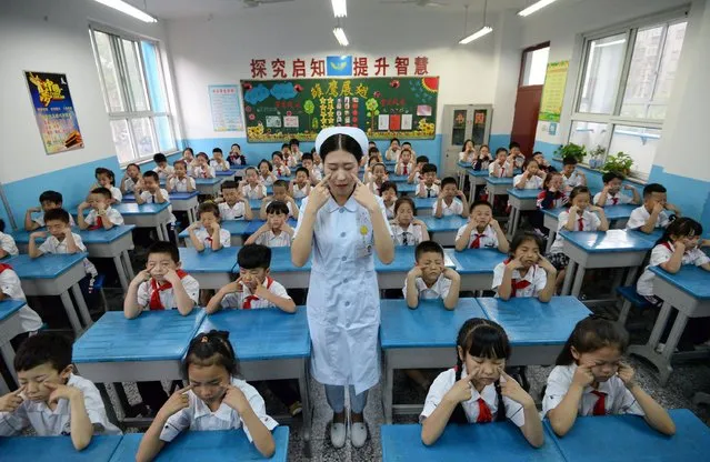 A hospital staff member teaches primary school children how to do eye exercises, at a primary school in Handan, in China's northern Hebei province on June 5, 2017. (Photo by AFP Photo/Stringer)