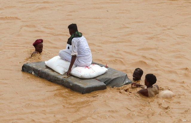 A person sits on bags of aid on a makeshift raft while others wade through flood water, following devastating floods, in South Tokar, Red Sea State, Sudan, on August 28, 2024. (Photo by El Tayeb Siddig/Reuters)