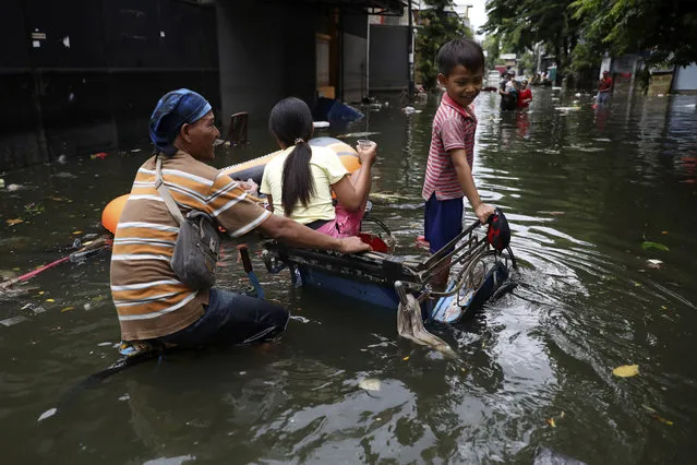 A young boy reacts as he rides on a tricycle with his father and sister at a flooded neighborhood in Jakarta, Indonesia, Saturday, January 4, 2020. (Photo by Dita Alangkara/AP Photo)