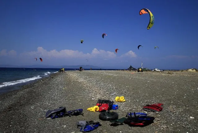 Kitesurfers are seen in the background as abandoned life-jackets used by refugees that arrived this morning are seen on a beach on the Greek island of Kos August 10, 2015. (Photo by Yannis Behrakis/Reuters)