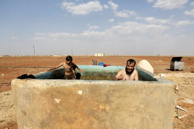 An Al-Furqan Brigade fighter (R) swims inside an irrigation pool with local children to cool down from summer heat, in Tel Mamo village, in the southern countryside of Aleppo, Syria June 23, 2016. (Photo by Khalil Ashawi/Reuters)