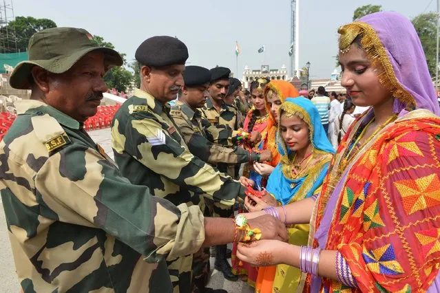 Indian school girls tie a sacred thread or rakhi onto the wrists of Indian Border Security Force (BSF) personnel during a ceremony observing the festival of Raksha Bandhan at the India-Pakistan Wagah Border Post about 35km from Amritsar on August 7, 2017. (Photo by Narinder Nanu/AFP Photo)