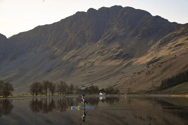 A paddle boarder is reflected in the early morning calm waters of Buttermere in the Lake District, United Kingdom on March 23, 2022. (Photo by Anna Gowthorpe/Rex Features/Shutterstock)