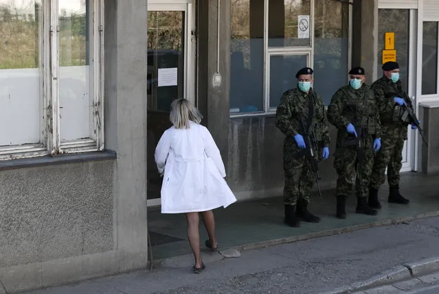 In this photo taken Monday, March 16, 2020, Serbian Army soldiers stand guard outside the Clinic for Infectious and Tropical Diseases in Belgrade, Serbia. Although the global COVID-19 pandemic has not hit Eastern and Central Europe with such a force compared to Italy, Spain and France, health officials throughout the region are sounding alarm about the lack of medical staff, facilities, equipment and enough hospital beds to handle several virus outbreaks simultaneously. (Photo by Darko Vojinovic/AP Photo)