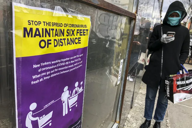 Signs displaying directions for maintaining social distancing due to COVID-19 concerns are posted on a supermarket as customers wait outside, Friday, April 10, 2020, in New York. (Photo by John Minchillo/AP Photo)