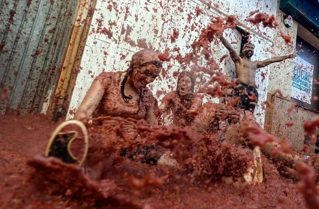 Revellers covered in tomato pulp sit on a crushed tomato flooded street as they take part in the annual “Tomatina” festival in the eastern town of Bunol, on August 31, 2022. “La Tomatina”, a famous tomato fight that attracts thousands of tourists to the town of Bunol (eastern Spain), made its comeback today after two years of absence due to the pandemic. Some 15,000 people took part in this food fight, with 130 tonnes of (very) ripe tomatoes as ammunition, according to figures provided by the town hall. (Photo by Jose Jordan/AFP Photo)