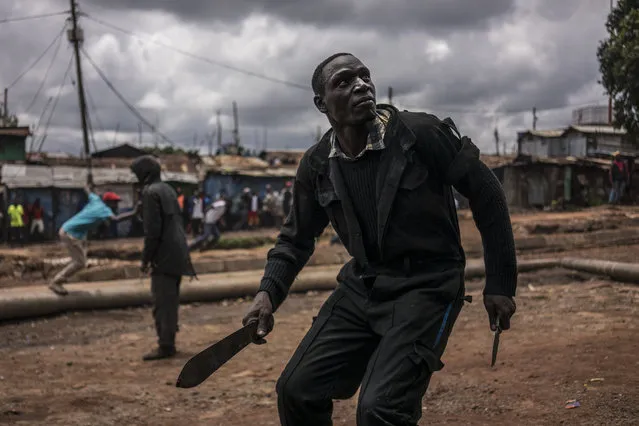 A protester brandishing a machete and a knife prepares to take cover from incoming tear gas canisters during clashes with police forces in Kibera, Nairobi, on October 26, 2017. Kenyans trickled into polling stations today for a repeat election that has polarised the nation, amid sporadic clashes as supporters of opposition leader ignored his call to stay away and tried to block voting. (Photo by Marco Longari/AFP Photo)
