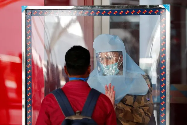 A member of the Central Industrial Security Force (CISF) talks with a passenger through a glass shield, after the government allowed domestic flight services to resume, during an extended nationwide lockdown to slow the spread of the coronavirus disease (COVID-19), at Indira Gandhi International (IGI) airport, in New Delhi, India, May 25, 2020. (Photo by Adnan Abidi/Reuters)