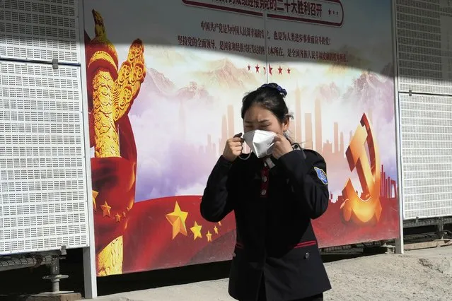 A woman wears a mask as she passes by propaganda for the upcoming 20th Party Congress to be held in Beijing, Monday, October 10, 2022. Chinese cities were imposing fresh lockdowns and travel restrictions after the number of new daily COVID-19 cases tripled during a weeklong holiday, ahead of the major Communist Party meeting in Beijing next week. (Photo by Ng Han Guan/AP Photo)