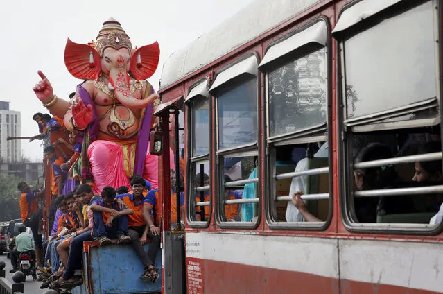 Devotees sit on a truck carrying an idol of elephant-headed Hindu god Ganesha from a workshop ahead of Ganesha Chaturthi festival in Mumbai, India, Wednesday, September 16, 2015. Ganesha Chaturthi, the 10-day festival that celebrates the birth of Ganesha, begins Sept. 17 and ends with the immersion of Ganesha statues in the Arabian Sea and other water bodies. (Photo by Rajanish Kakade/AP Photo)