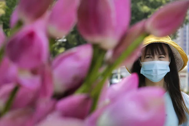 A woman wearing a face mask to protect against the new coronavirus walks by lotus flowers on sale on a street in Beijing, Wednesday, July 22, 2020. (Photo by Andy Wong/AP Photo)