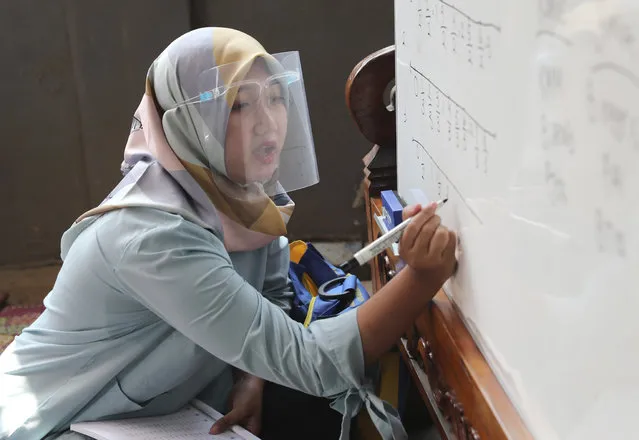 Teacher Inggit Andini, wearing a face shield as a precaution against the coronavirus outbreak, teaches at a makeshift class at her home in Tangerang, Indonesia, Monday, August 10, 2020. Andini offered free extra lessons for students who lack access to the internet as the school where she works at remain closed and switched to online learning due to the outbreak. (Photo by Tatan Syuflana/AP Photo)
