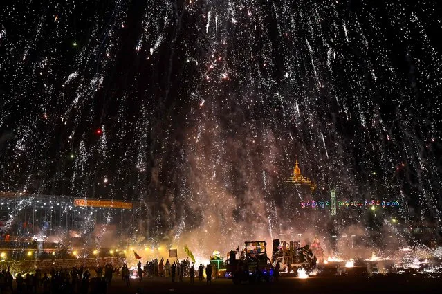 This photo taken on November 7, 2022 shows revellers celebrating as fireworks explode after they released a hot-air balloon attached with fireworks during the Tazaungdaing Lighting Festival at Pyin Oo Lwin Township in Mandalay. Thousands of people have gathered in the hills of central Myanmar for the annual Tazaungdaing light festival that marks the end of the rainy season with a fiery nighttime display of exploding hot-air balloons. (Photo by AFP Photo/Stringer)