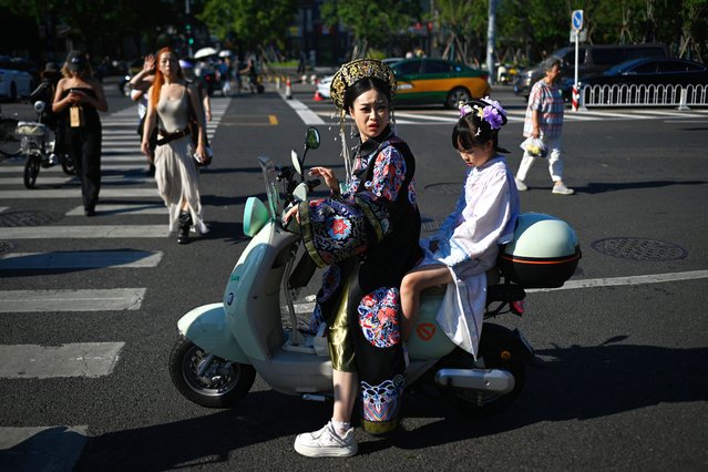 A woman and child clad in traditional attire ride an electric scooter in Beijing on August 25, 2025. (Photo by Wang Zhao/AFP Photo)