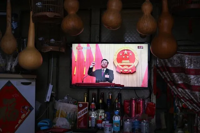A TV screen at a convenience store shows live coverage as Chinese President Xi Jinping swears an oath after being re-elected as president for a third term during the third plenary session of the National People's Congress (NPC) in Beijing on March 10, 2023. (Photo by Greg Baker/AFP Photo)