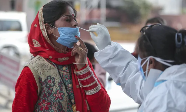 A health worker collects a swab sample from a woman to test for COVID-19 by a road side in Jammu, India, Monday, December 7, 2020. India is second behind the U.S. in total coronavirus cases but has one of the lowest deaths per million population globally. (Photo by Channi Anand/AP Photo)