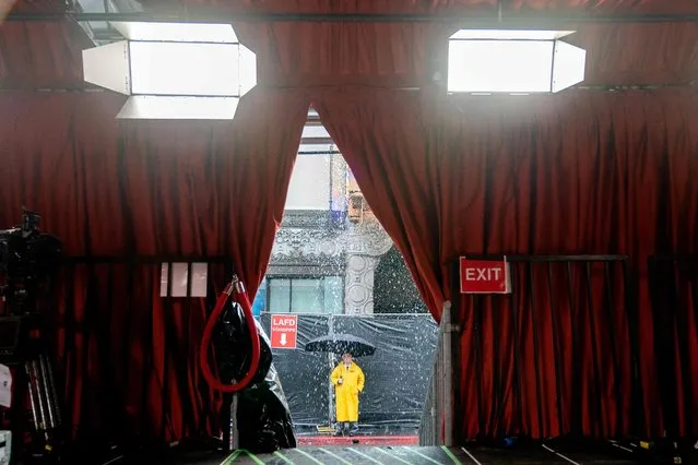 A security guard stands in the rain as preparations are made along the red carpet arrivals area, ahead of the 95th Academy Awards, in Hollywood, California, on March 10, 2023. The red carpet for the Oscars airing on March 12, 2023, is champagne-color for 2023. (Photo by Stefani Reynolds/AFP Photo)