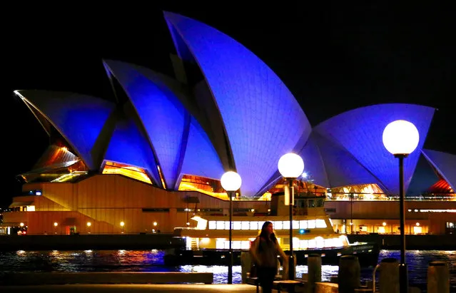 A pedestrian and ferry can be seen in front of the Sydney Opera House as it is illuminated blue as part of an event to mark the annual Blue Knot Day which raises awareness of adult survivors of childhood trauma and abuse in Australia, October 24, 2016. (Photo by David Gray/Reuters)
