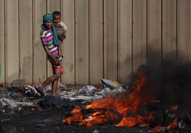 A Filipino scavenger carries his son amid black smoke billowing from electrical wires being burned by scavengers at a dumpsite in Manila, Philippines on Thursday, January 8, 2015. Scavengers earn about P150 (US $3) a day by selling recyclable scraps, copper and other metals they find in the heap of garbage. (Photo by Aaron Favila/AP Photo)