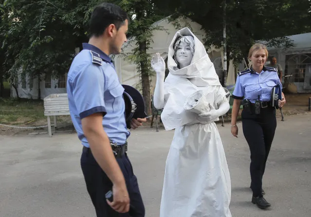 In this Thursday, May 24, 2018, photograph, an artist of Ukraine's Artel Myth, walks by Romanian police officers, before performing her Concordia character during the Living Statues International Festival, in Bucharest, Romania. Wait, did that statue really move? It may have been the question many themselves while taking a walk in Bucharest over the past week, during the International Living Statues Festival. (Photo by Vadim Ghirda/AP Photo)