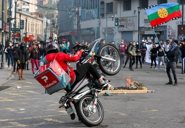 The driver of a delivery service performs with his motorcycle in front of protesters gathered ahead of the one-year anniversary of mass protests that saw thousands of Chileans take to the streets, in Valparaiso, Chile on October 16, 2020. (Photo by Rodrigo Garrido/Reuters)