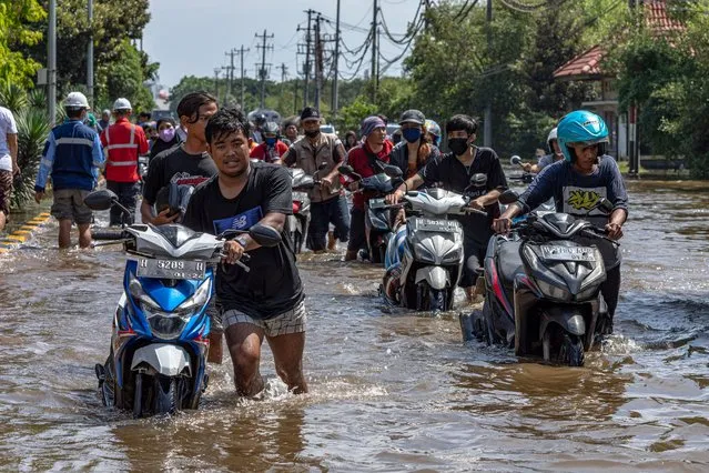 Workers push their motorbike through the water at Tanjung Emas container port terminal area which got flooded following high tides and broken seawalls, in Semarang, Central Java province, Indonesia on May 24, 2022. (Photo by Aji Styawan/Antara Foto via Reuters)