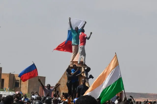 Protesters wave Nigerien and Russian flags as they gather during a rally in support of Niger's junta in Niamey on July 30, 2023. Thousands of people demonstrated in front of the French embassy in Niamey on Sunday, before being dispersed by tear gas, during a rally in support of the military putschists who overthrew the elected president Mohamed Bazoum in Niger. Before the tear-gas canisters were fired, a few soldiers stood in front of the embassy to calm the demonstrators. (Photo by AFP Photo/Stringer)