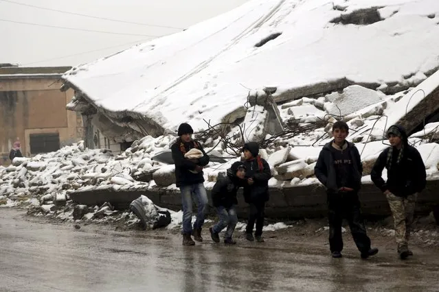 Boys walk past damaged buildings covered with snow in the rebel-controlled area of Maaret al-Numan town in Idlib province, Syria, January 5, 2016. (Photo by Khalil Ashawi/Reuters)