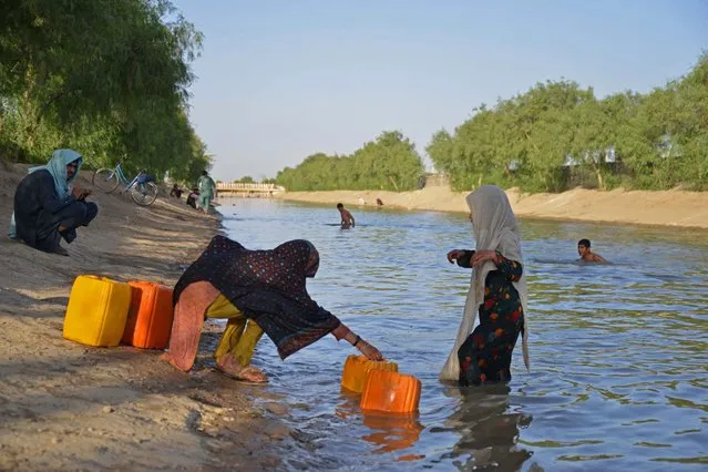 Afghan girls fill containers with water from a canal on the outskirts of Kandahar on July 16, 2023. (Photo by Sanaullah Seiam/AFP Photo)